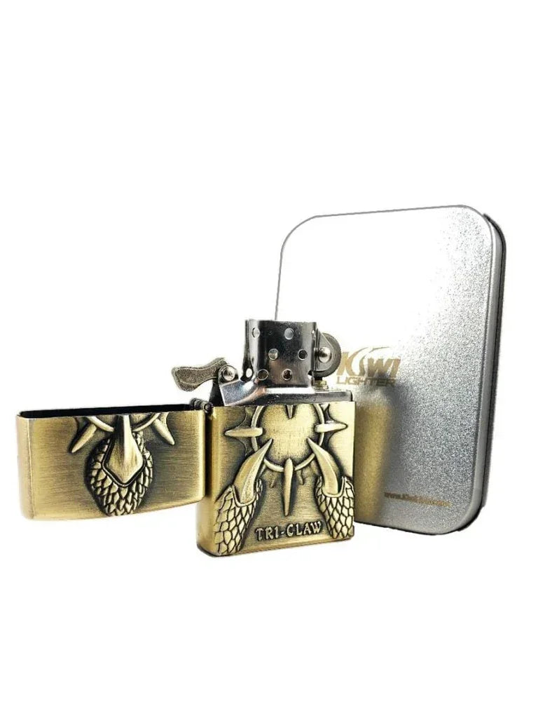 Antique brass flint lighter with dragon claw design and 'TRI-CLAW' engraving, next to silver metal case