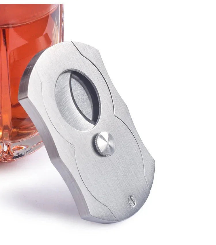 stainless steel cigar cutter with double guillotine blades beside glass of brown liquor