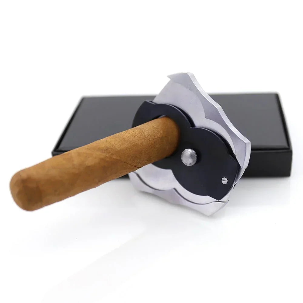 Cigar with a decorative black and silver cigar cutter on a white surface with a black box in background