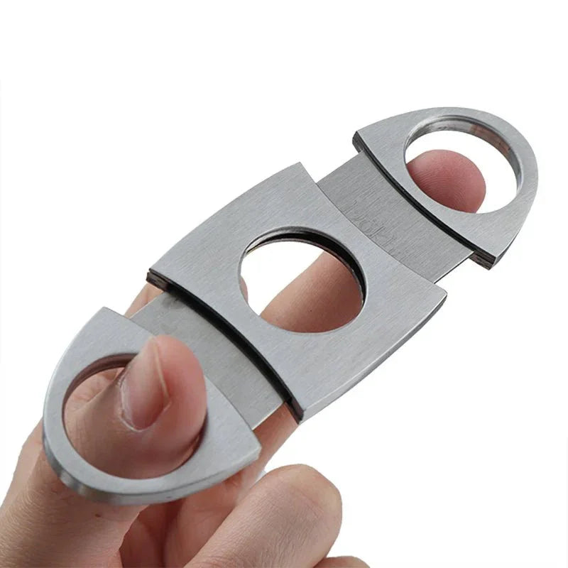 Hand holding stainless steel cigar cutter with circular finger holes on white background